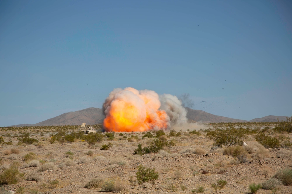 Military vehicle creating a large explosion in a desert landscape.