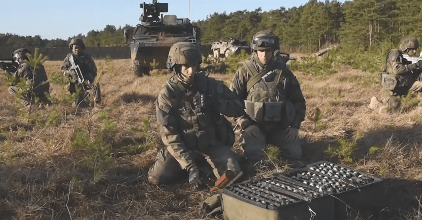 Soldiers kneeling in a field near open cases of military equipment.