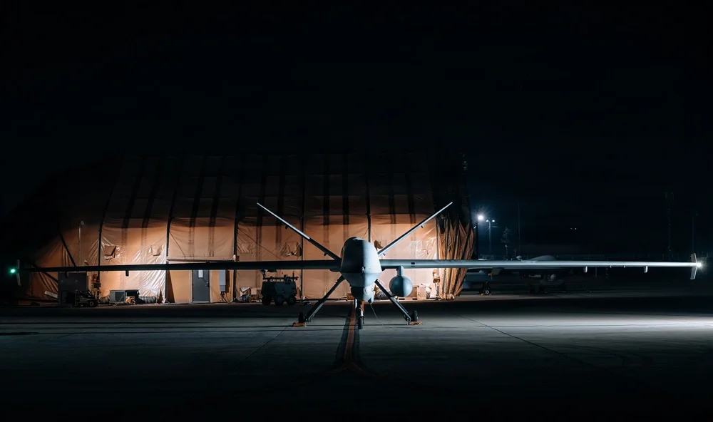 Large military drone parked on a runway at night.