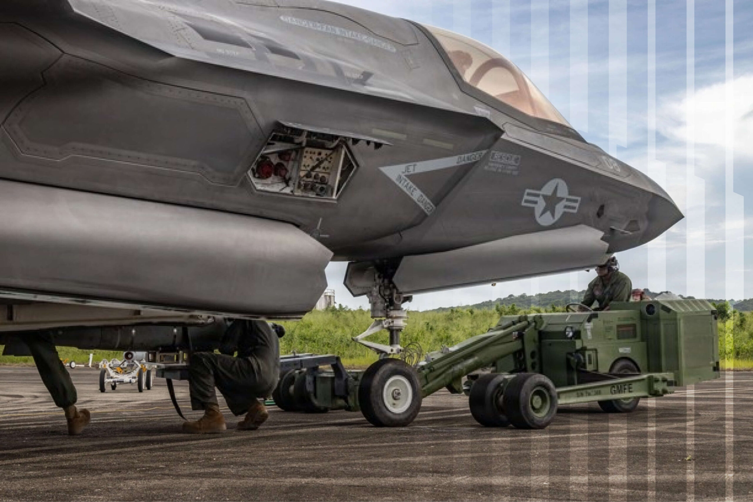 Ground crew performing maintenance and loading equipment onto a parked F-35 fighter jet on a runway.