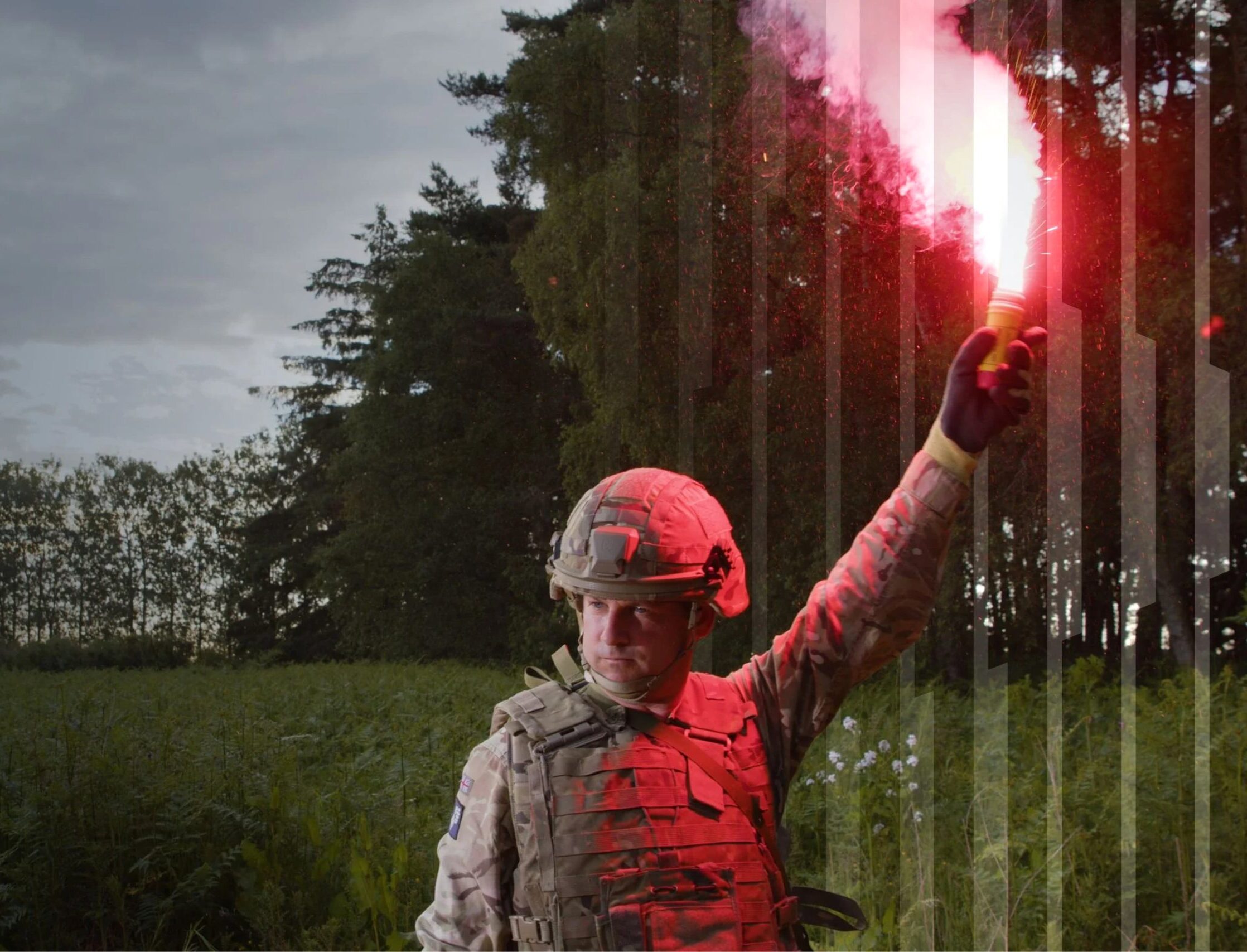 A soldier in camouflage gear holding a bright red signal flare aloft in a field.