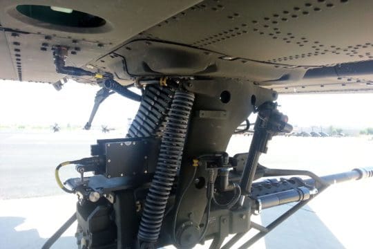 Close-up of a chin-mounted gun on an attack helicopter, showing the mechanical components and ammunition feed.