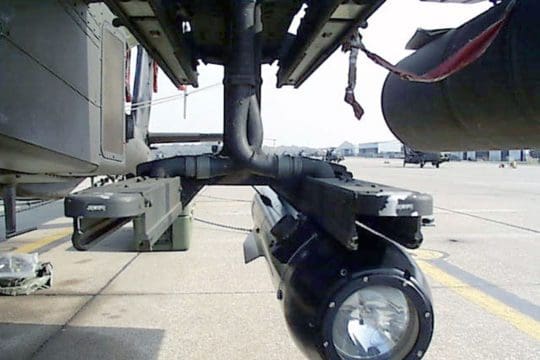 A missile attached to a launcher rail under a helicopter wing.