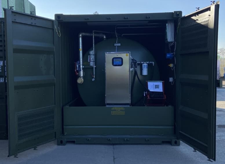 Green industrial storage tank with integrated dispensing hardware inside a shipping container.